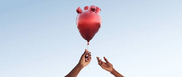 A hand passing a heart-shaped balloon to another hand
